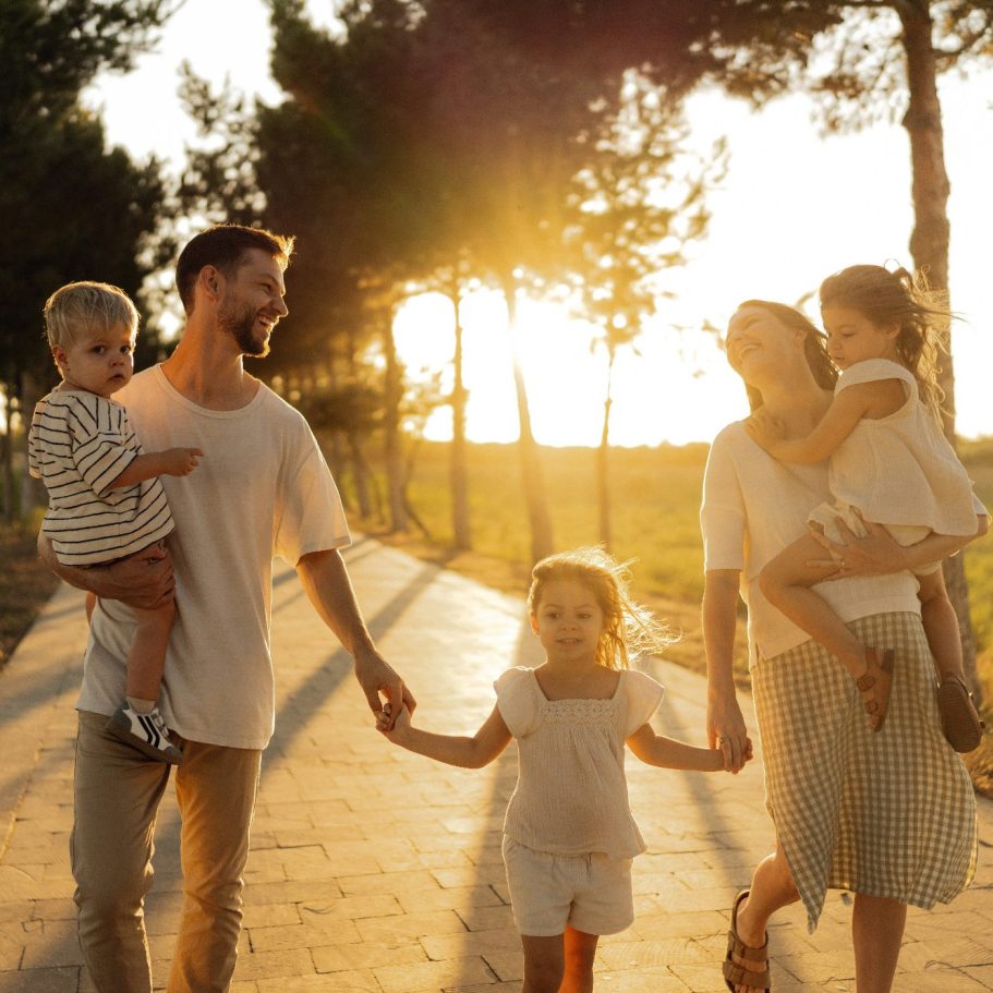 Familie spaziert zusammen bei Sonnenuntergang an einem Baum entlang.