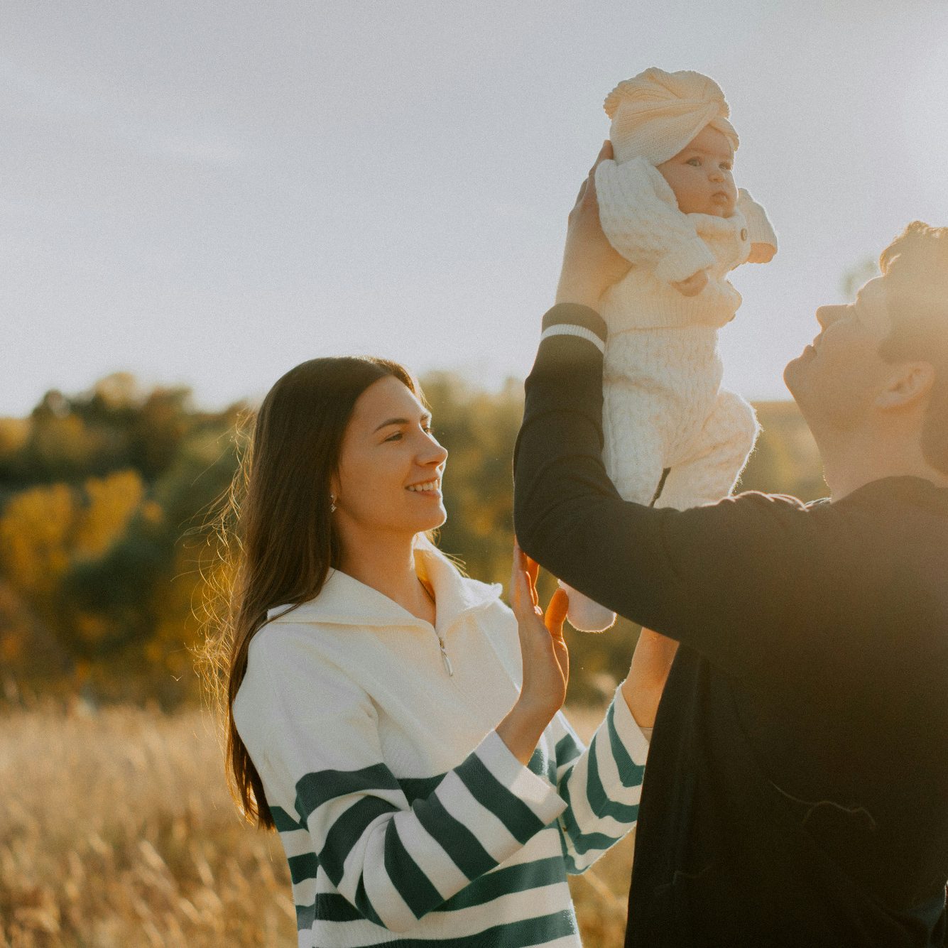 Eine Frau und ein Mann halten ein Baby im Freien vor einer herbstlichen Landschaft.